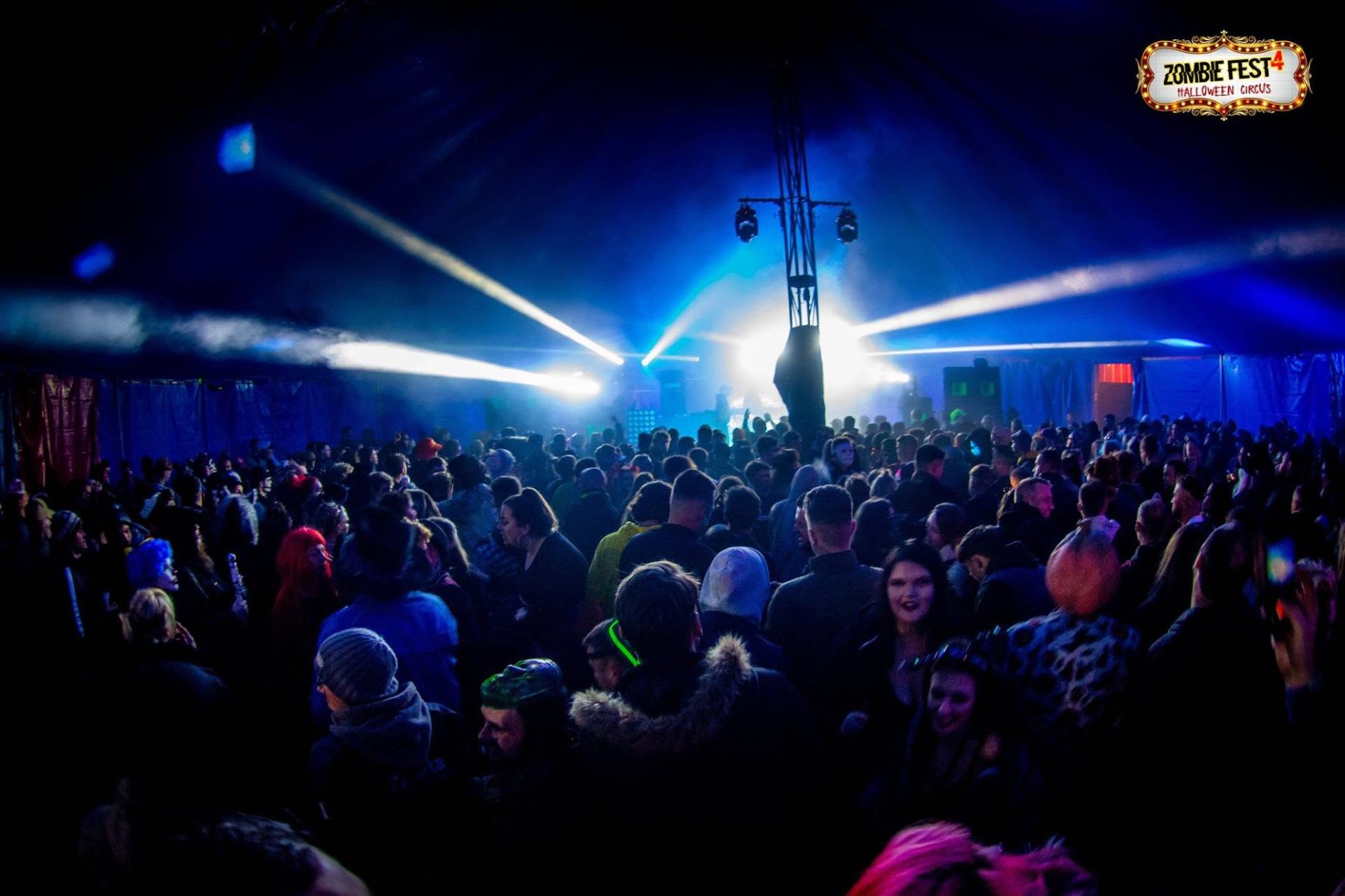 Packed crowd inside the Zombie Fest 4 Halloween Circus big top with blue beam lighting