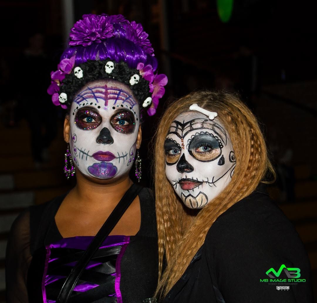 Two guests in intricate Day of the Dead sugar-skull face paint with purple floral headdress at Zombie Fest