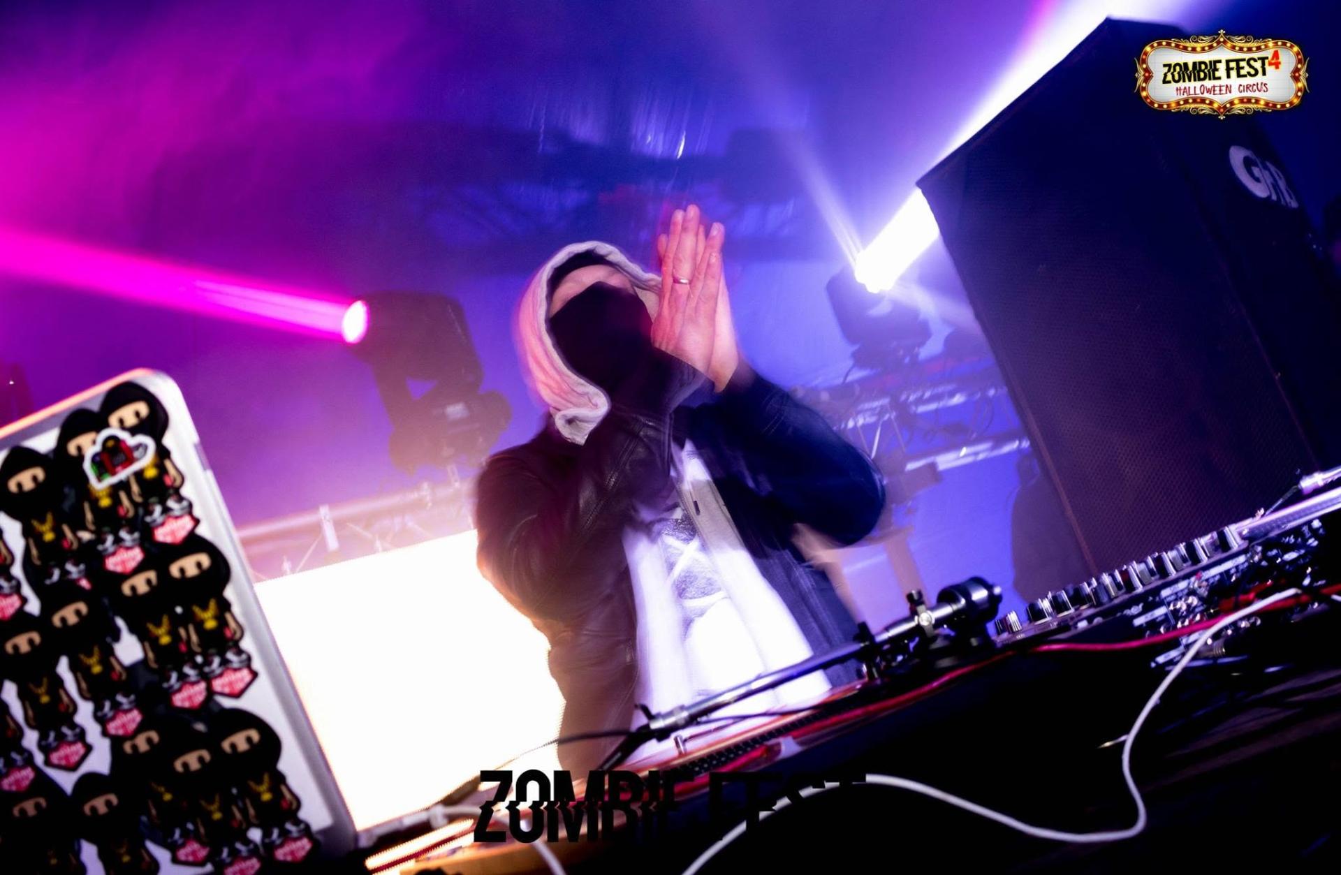 Jag Skills behind the decks with hands raised under purple lights at Zombie Fest 4 Halloween Circus